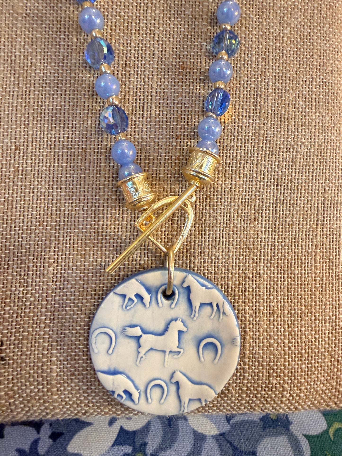 Round Ceramic Horse themed pendant hanging from a Stirrup toggle clasp All Srung on beautiful blue beads