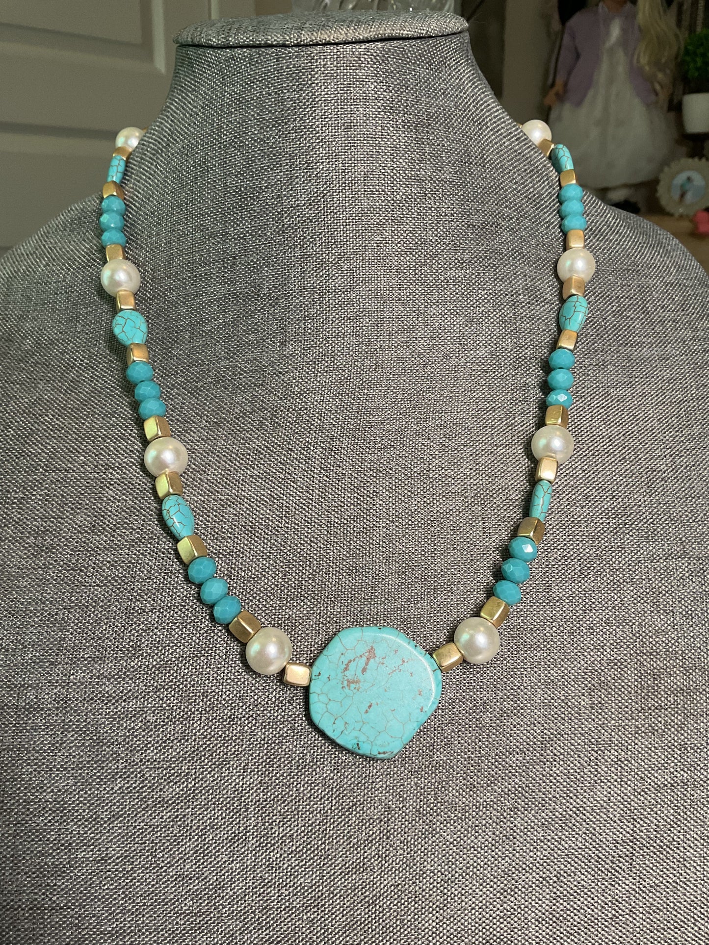 A turquoise, gold and pearl beaded necklace with large turquoise bead focal point