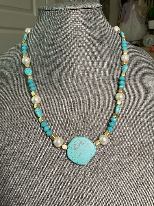 A turquoise, gold and pearl beaded necklace with large turquoise bead focal point