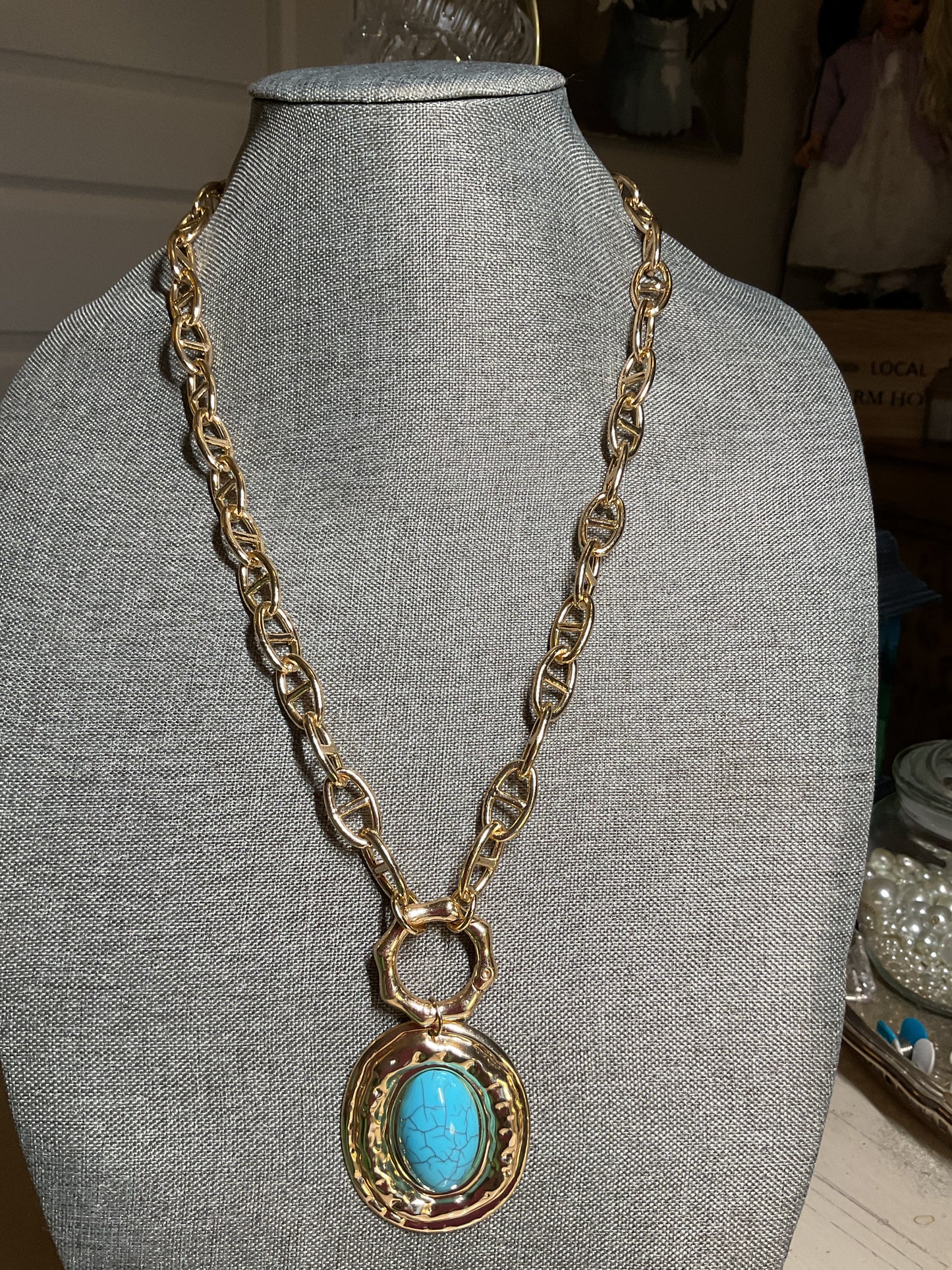 A long, chunky gold tone chain with a large turquoise and gold pendant
