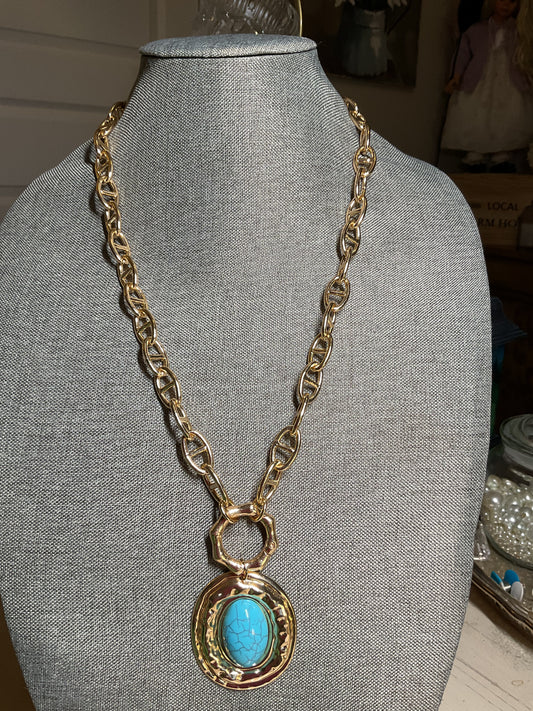 A long, chunky gold tone chain with a large turquoise and gold pendant