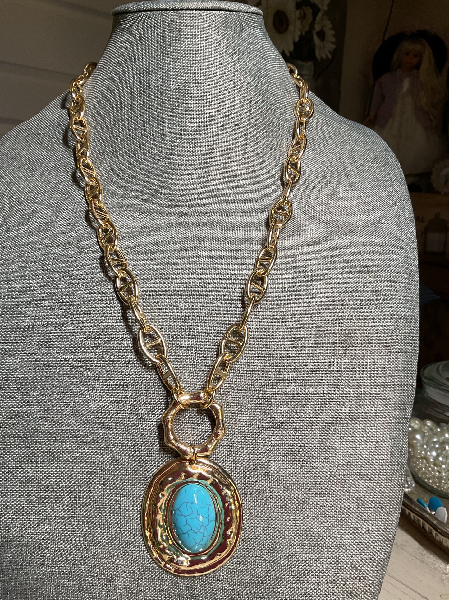 A long, chunky gold tone chain with a large turquoise and gold pendant