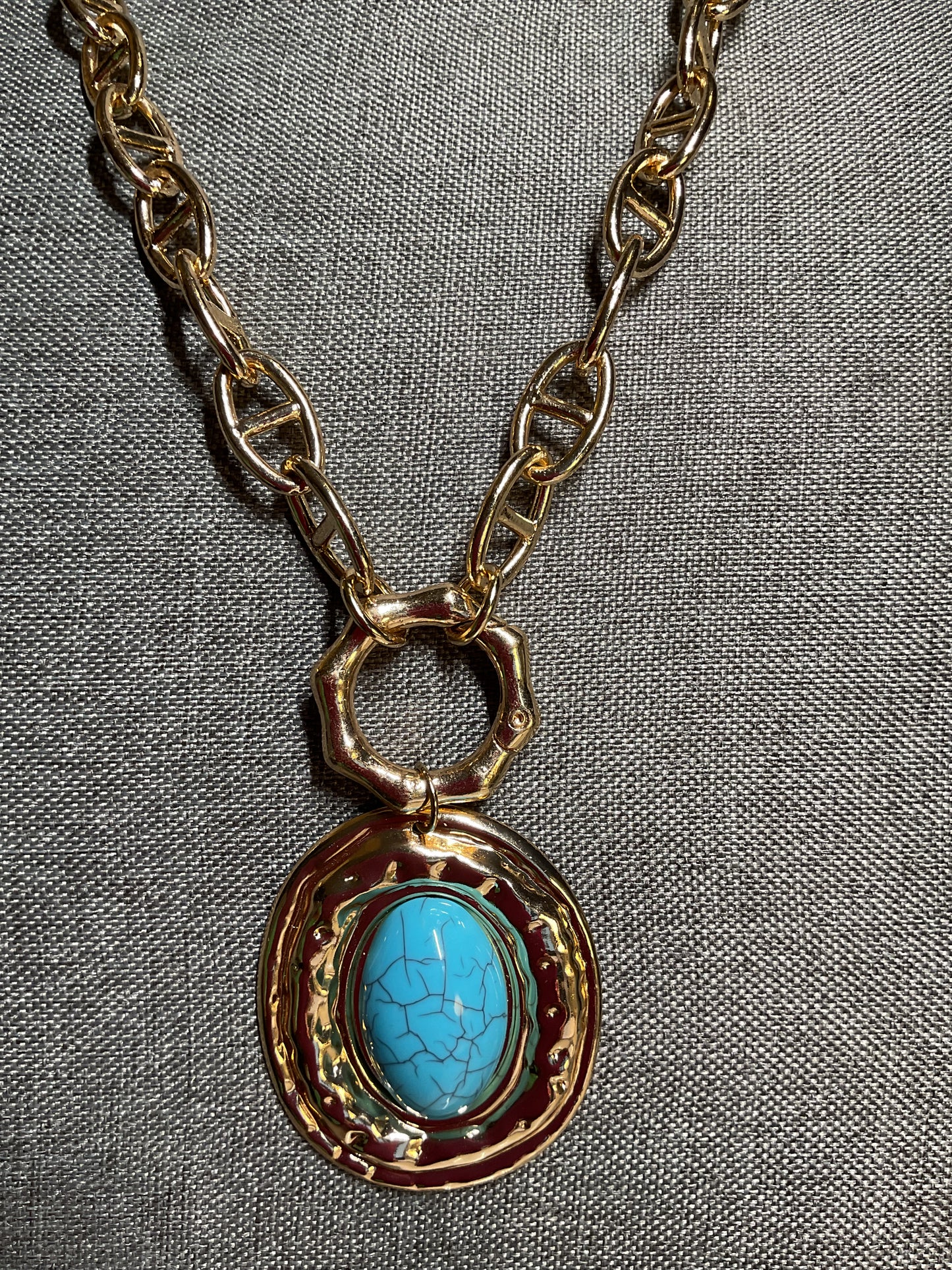A long, chunky gold tone chain with a large turquoise and gold pendant