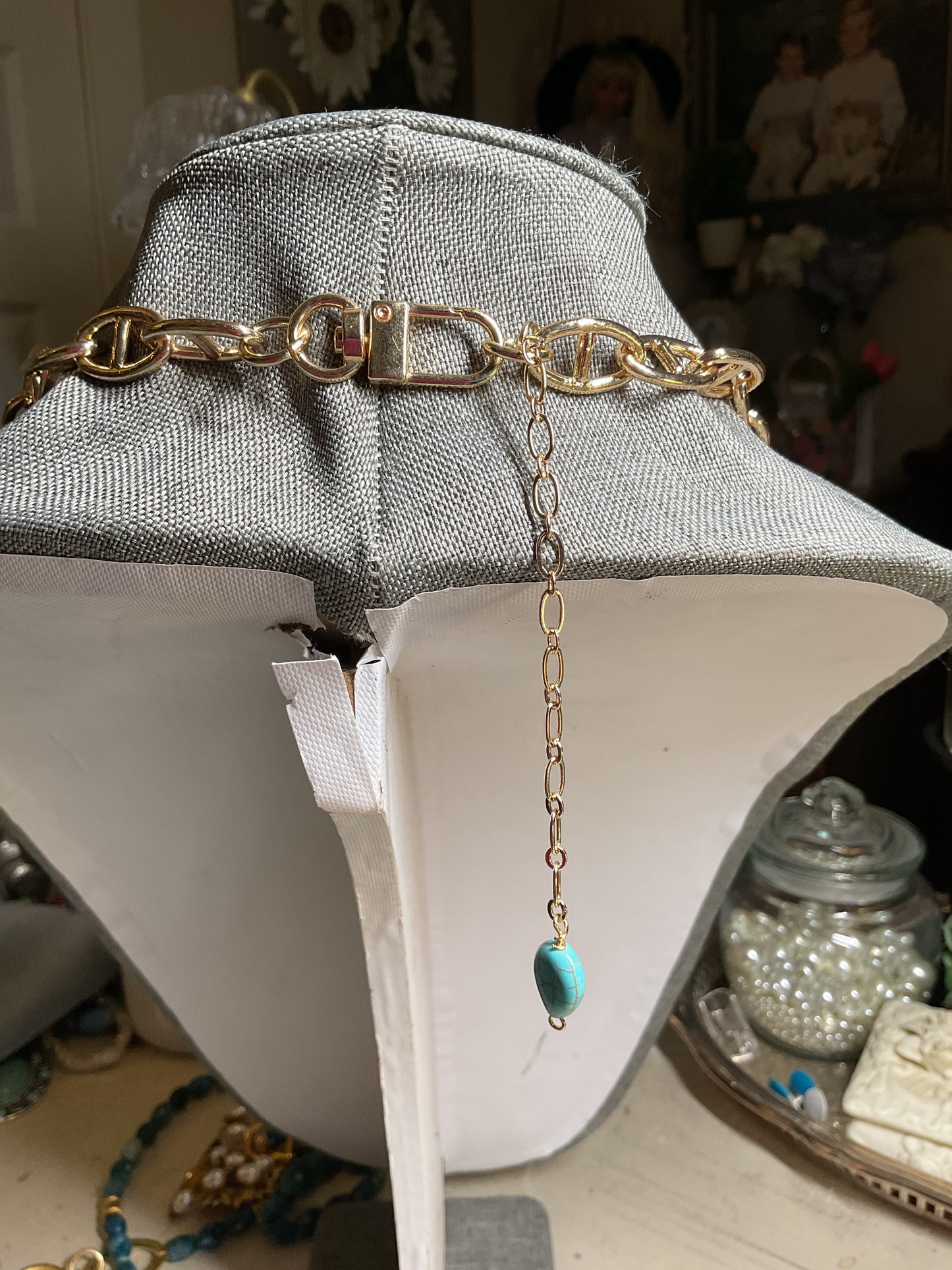 A long, chunky gold tone chain with a large turquoise and gold pendant