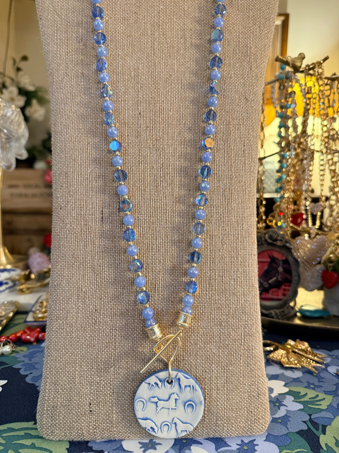 Round Ceramic Horse themed pendant hanging from a Stirrup toggle clasp All Srung on beautiful blue beads