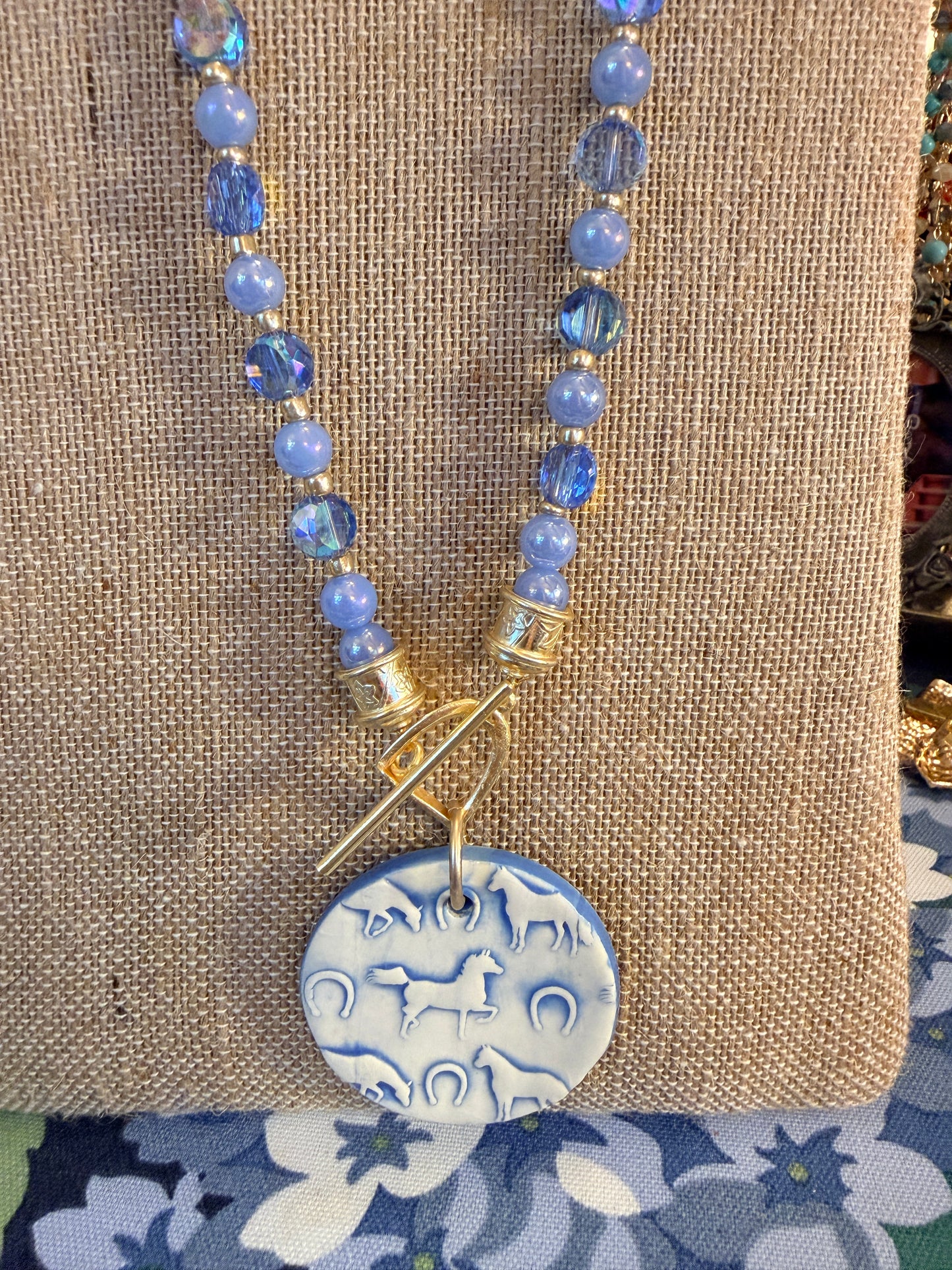 Round Ceramic Horse themed pendant hanging from a Stirrup toggle clasp All Srung on beautiful blue beads